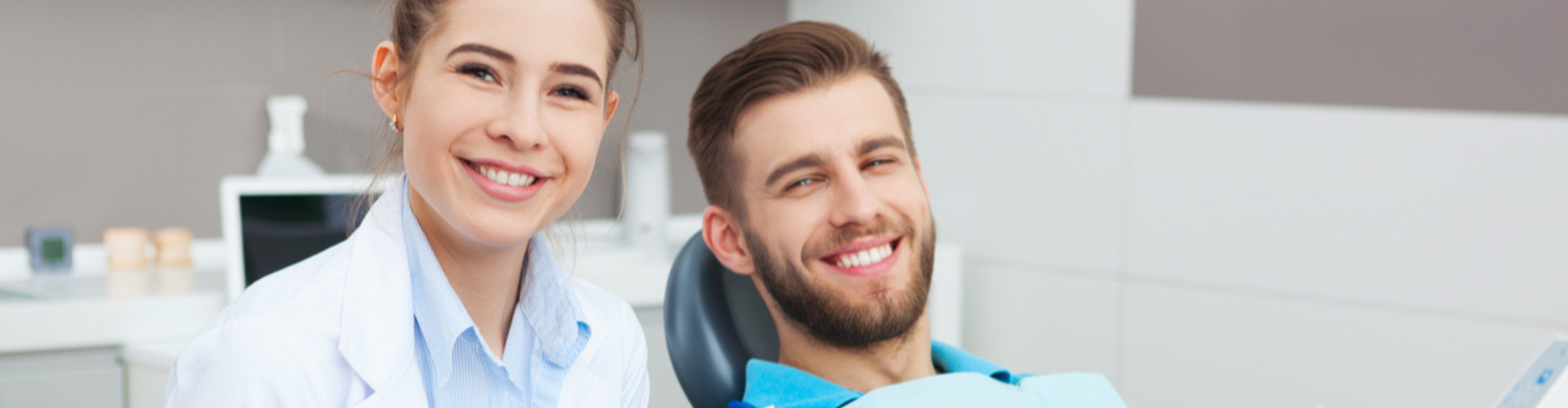 A dentist with a patient sitting in the dentist chair, both smiling at the camera.